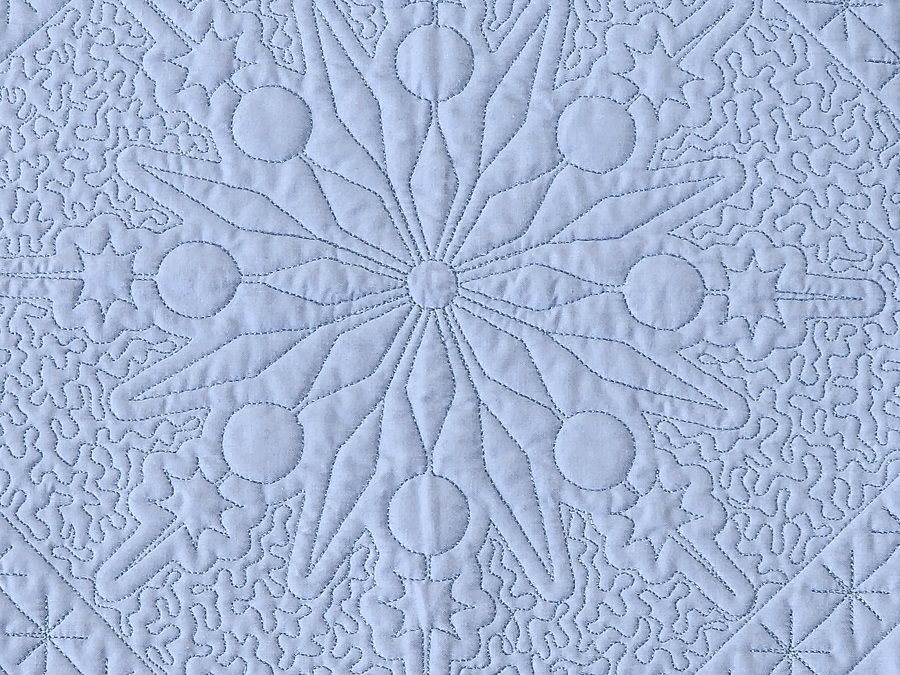 blue wholecloth quilt stitched with a snowflake motif surrounded by an echo and stippling