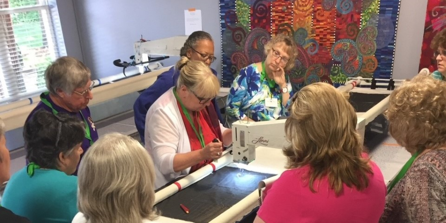 longarm quilting students surrounding an instructor quilting on an APQS longarm